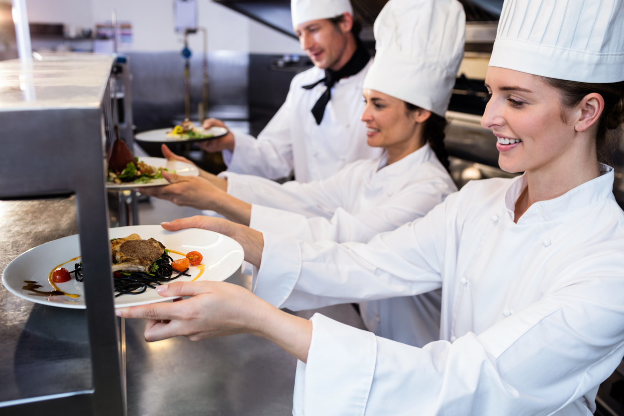 Chefs handing dinner plates through order station